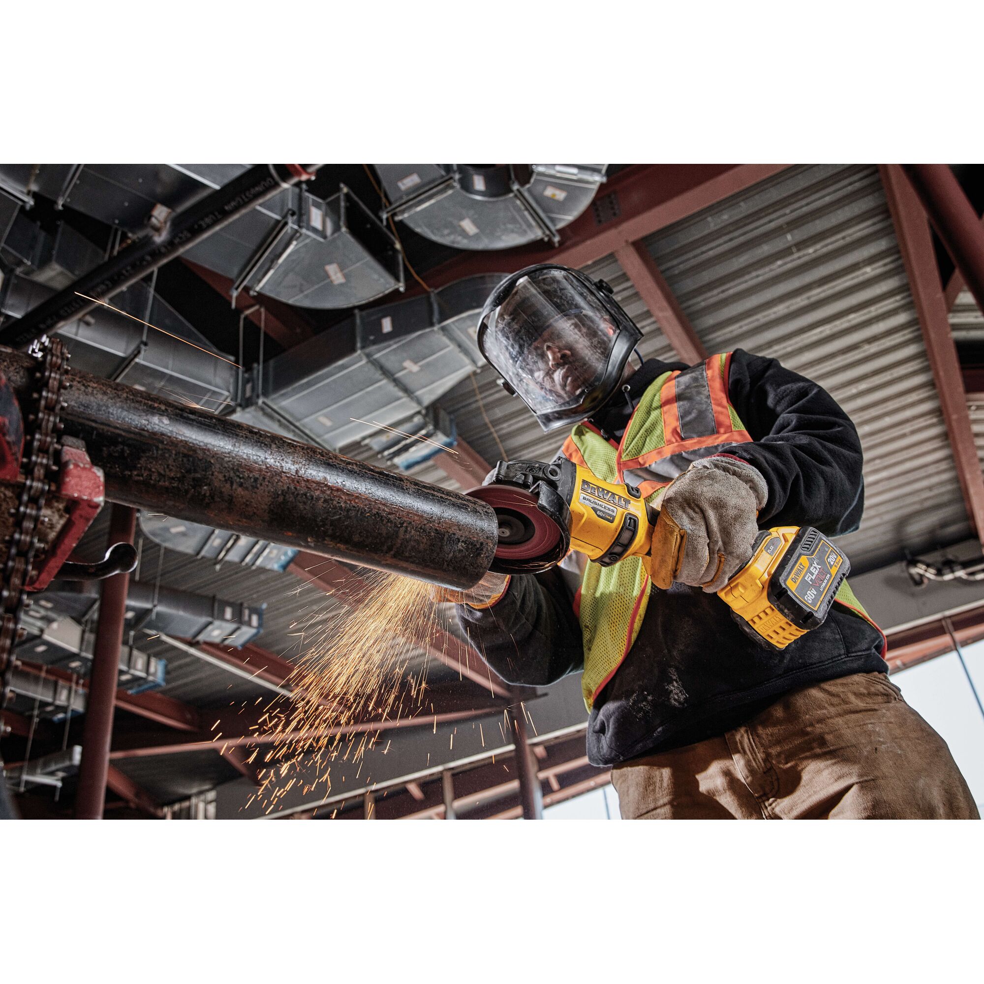 Worker using a DEWALT cordless grinder on a metal pipe, wearing safety gear. Sparks flying during operation.