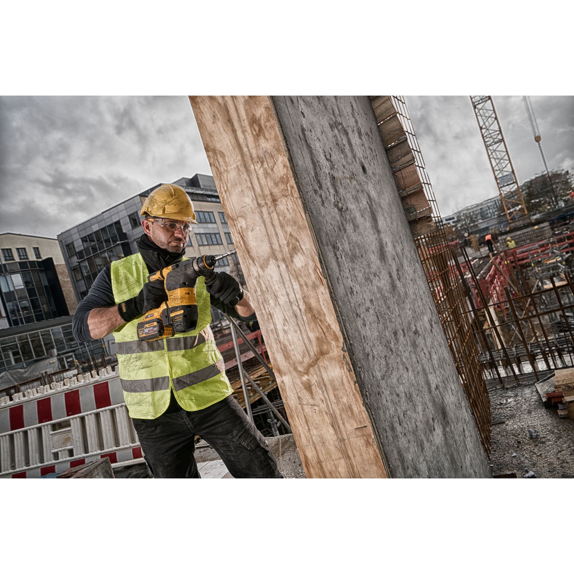 Worker uses DEWALT power tool to drill into concrete at a construction site, wearing helmet and safety vest.