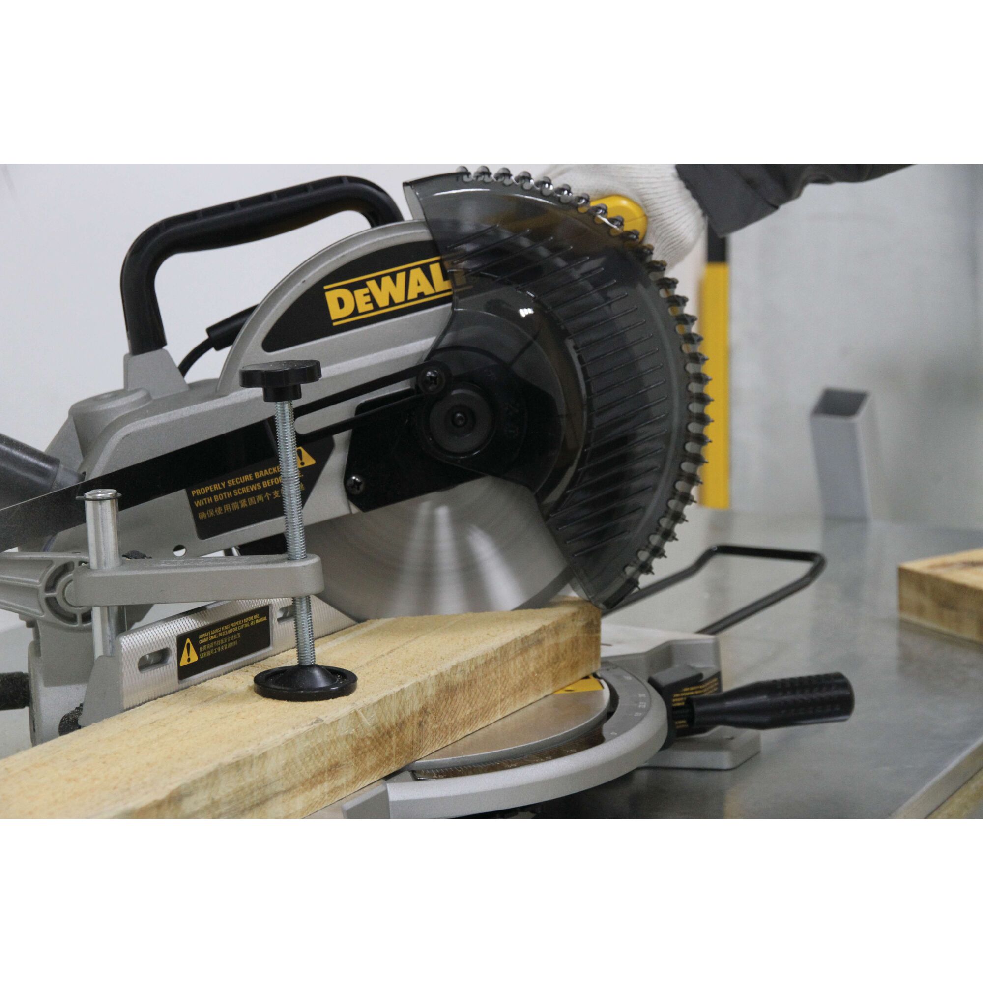A DEWALT miter saw cutting a wooden plank, with a gloved hand operating the saw in a workshop setting.