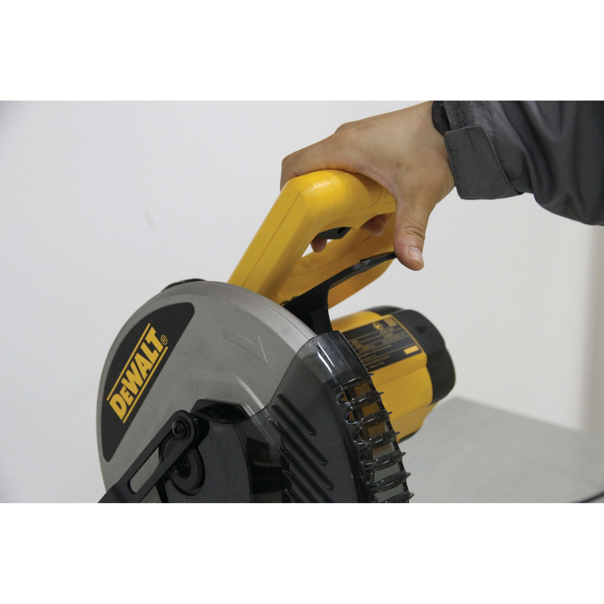A close-up of a person's hand gripping the yellow handle of a DEWALT circular saw.