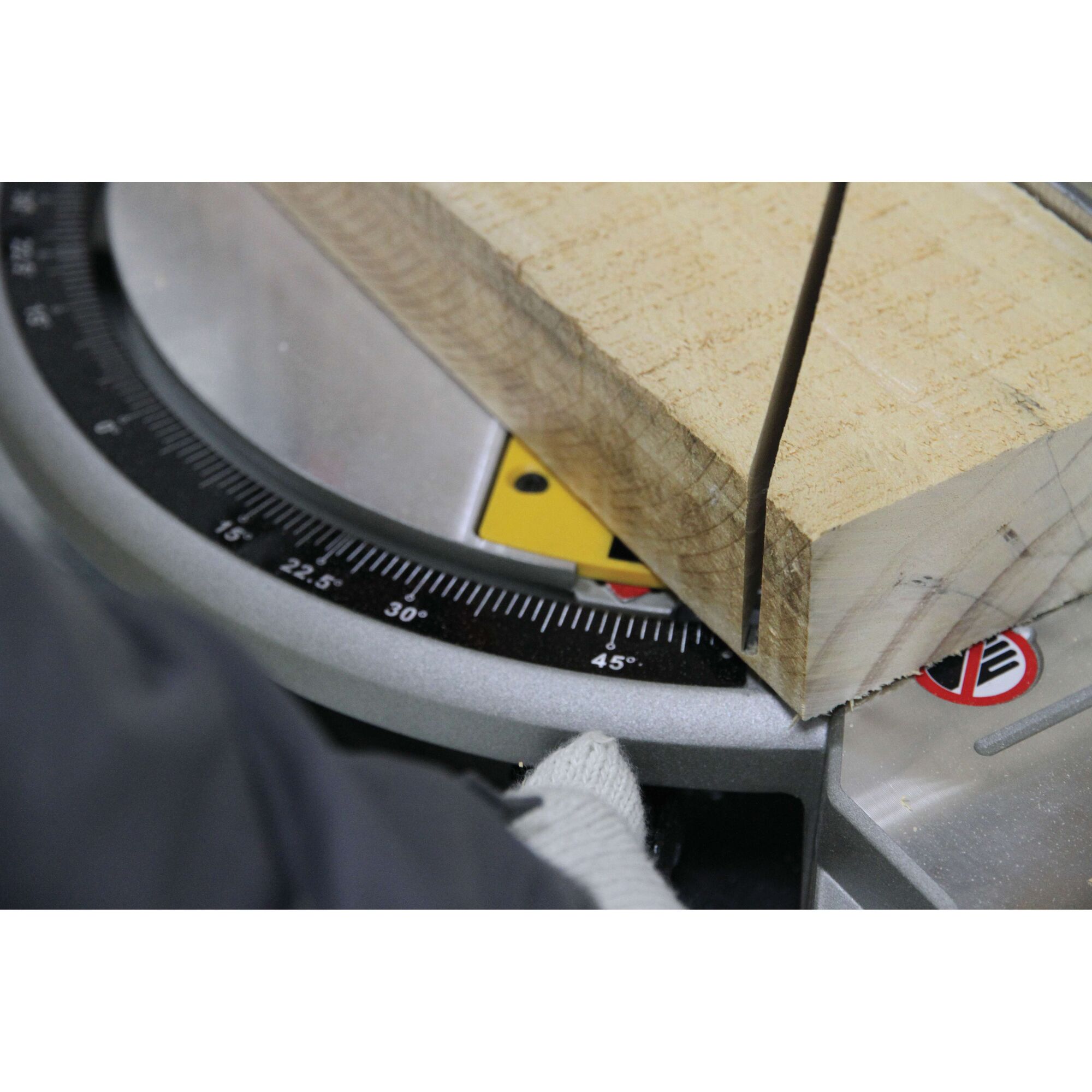 Close-up of a piece of wood being cut at a precise angle on a DEWALT miter saw. The angle gauge is clearly visible, and a gloved hand is adjusting the saw.