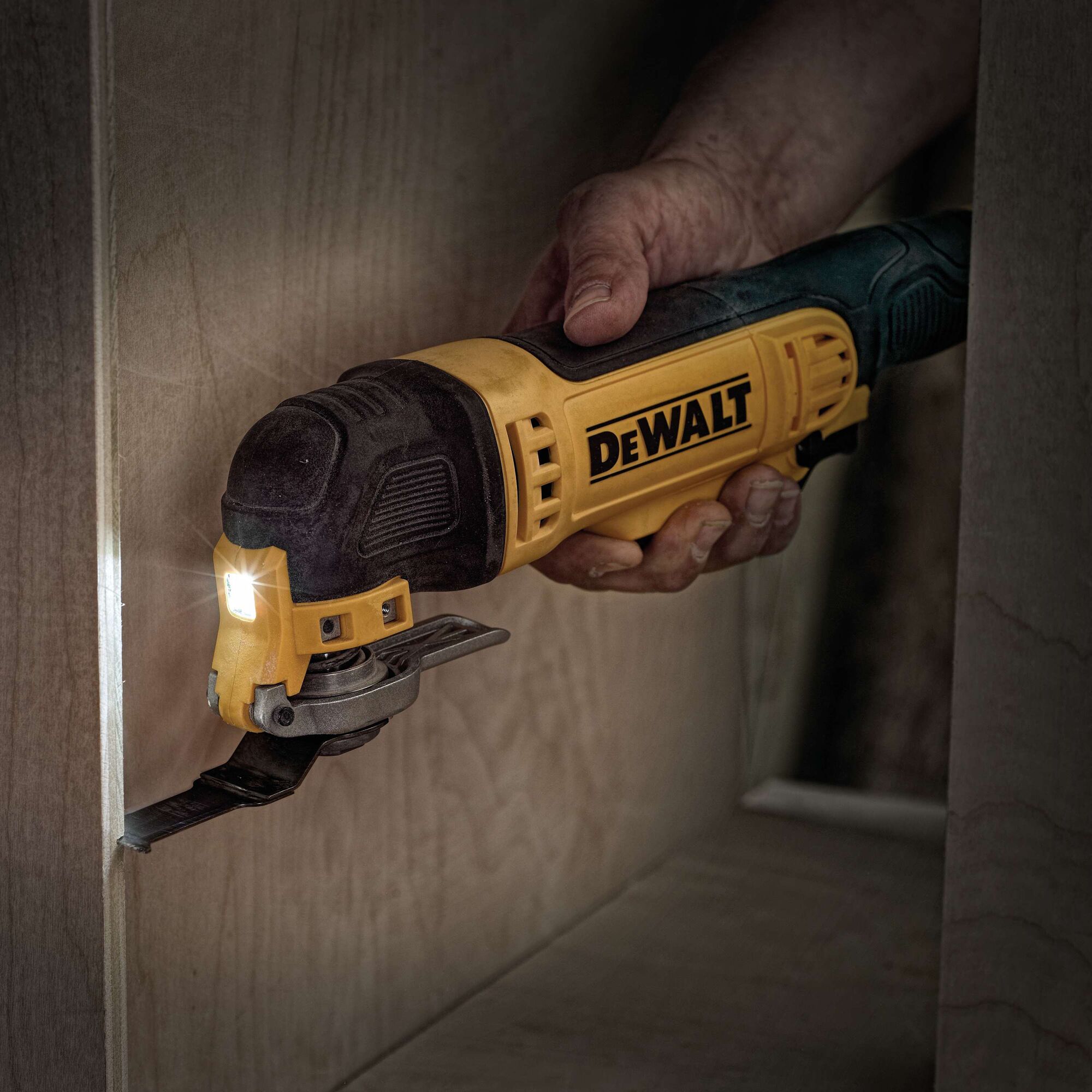 A hand using a DEWALT DWE315 multi-tool with a built-in LED light to cut into a piece of wood.