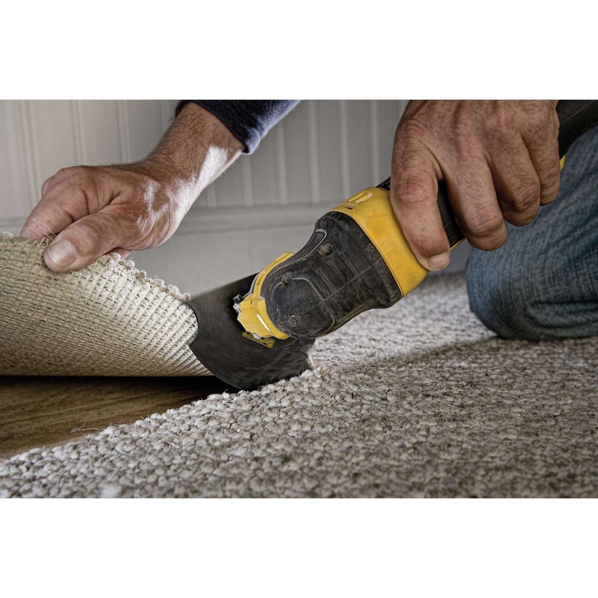 A close-up of a person using a DEWALT oscillating multi-tool to cut carpeting near the edge of a room.
