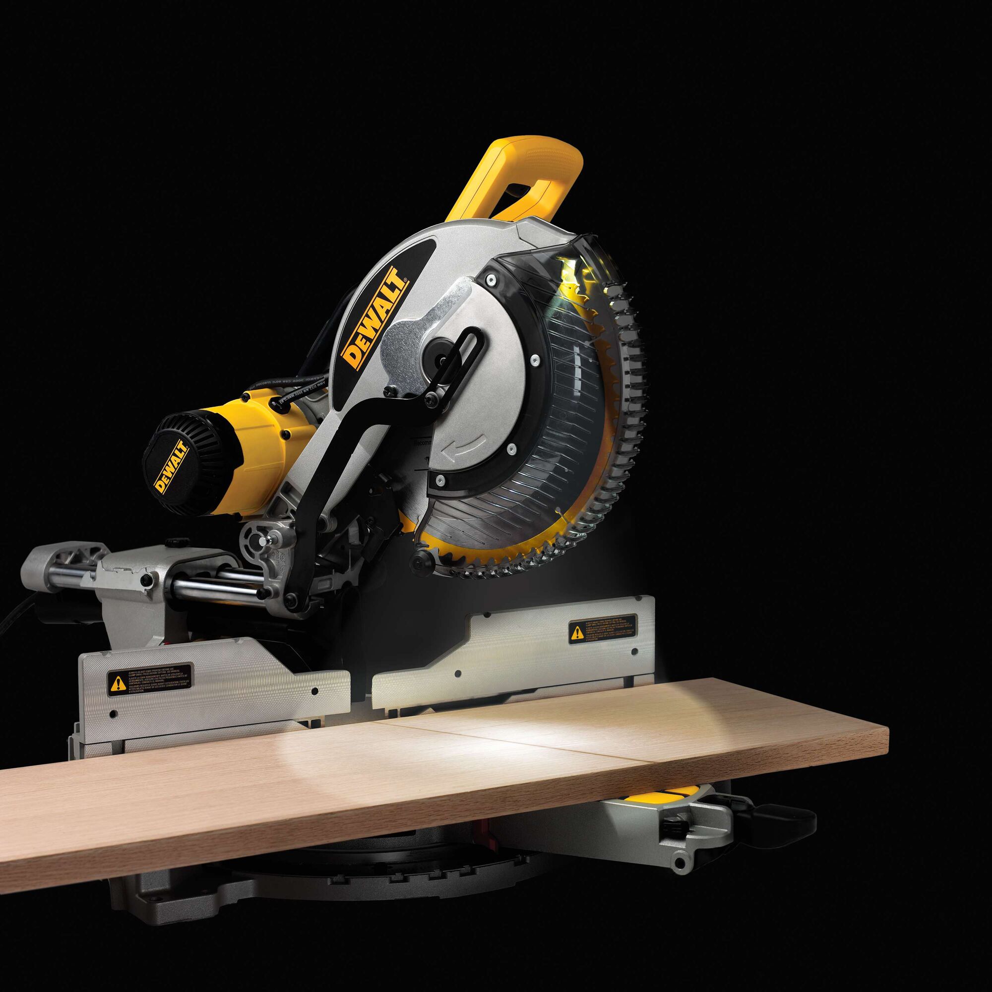 A DEWALT DWS780 miter saw, shown cutting a wooden plank. The saw features a prominent yellow and black design with visible safety warnings and adjustment controls. The background is black, highlighting the tool's details.